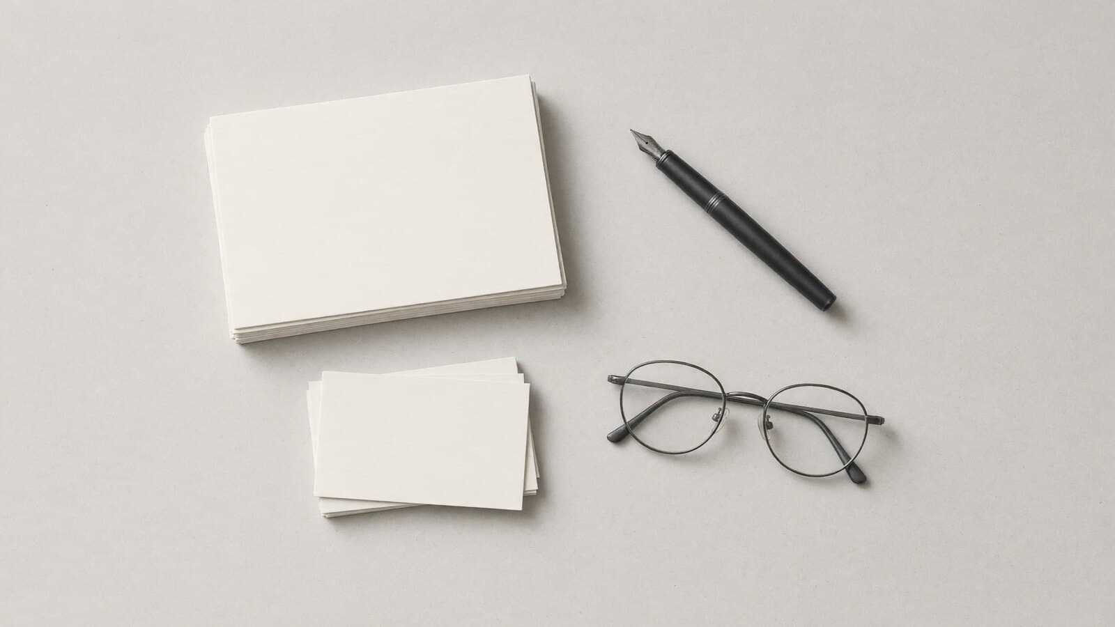A desk seen from above: a stack of blank paper, a fountain pen and reading glasses.