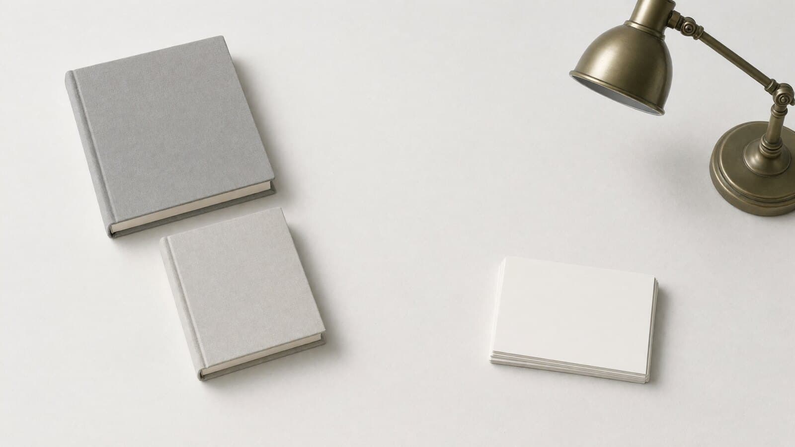 A reading desk seen from above: two closed cloth-bound books, index cards and a brass lamp.